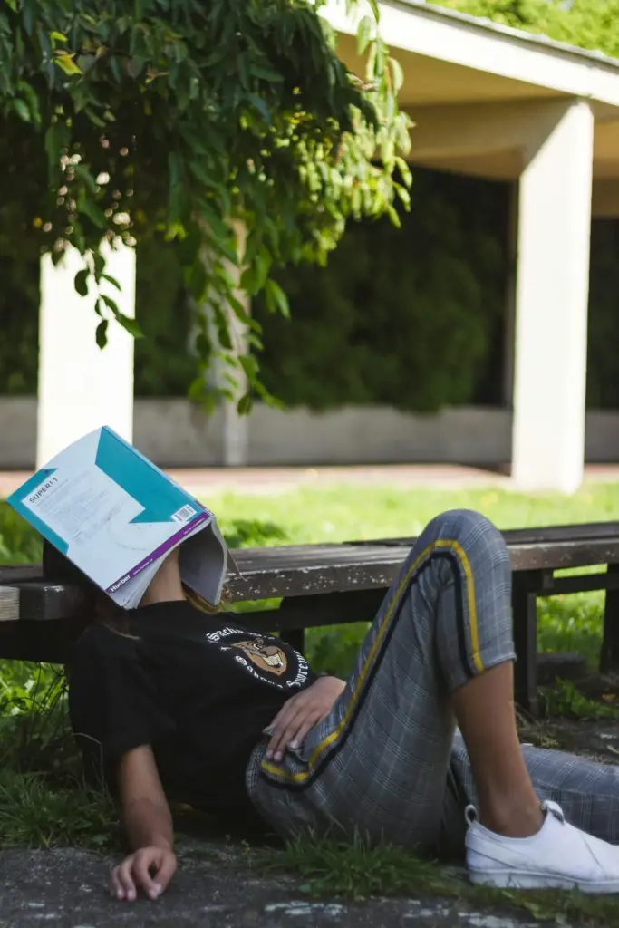 Jugendliche liegt auf einer Bank, ein Lehrbuch über dem Gesicht